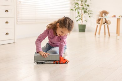 Photo of Little girl playing with toy car on floor at home, space for text