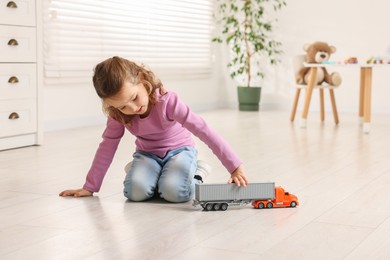 Photo of Little girl playing with toy car on floor at home