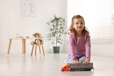 Photo of Little girl playing with toy car on floor at home, space for text