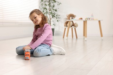 Photo of Little girl playing with toy car on floor at home, space for text