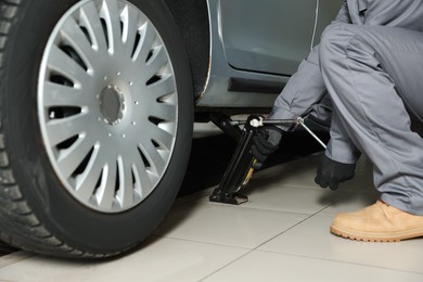 Photo of Car lifted by scissor jack. Auto mechanic changing wheel at service station, closeup