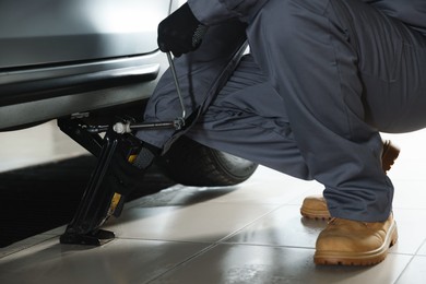 Photo of Auto mechanic lifting car with scissor jack at service station, closeup