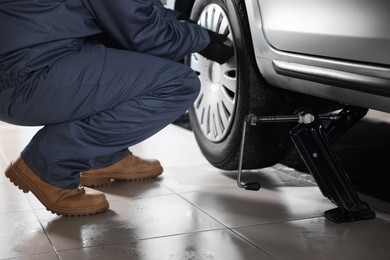 Photo of Car lifted by scissor jack. Auto mechanic changing wheel at service station, closeup