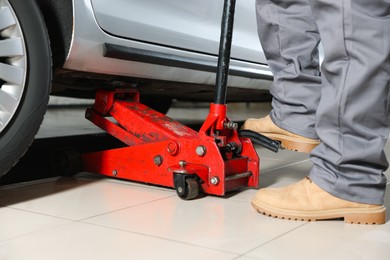 Photo of Auto mechanic lifting car with scissor jack at service station, closeup