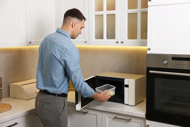 Photo of Man putting container with lunch into microwave in kitchen