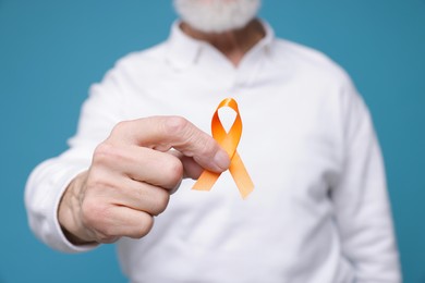 Photo of Multiple Sclerosis awareness. Senior man with orange ribbon on light blue background, closeup