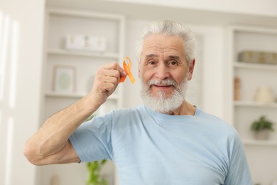 Photo of Multiple Sclerosis awareness. Senior man with orange ribbon indoors