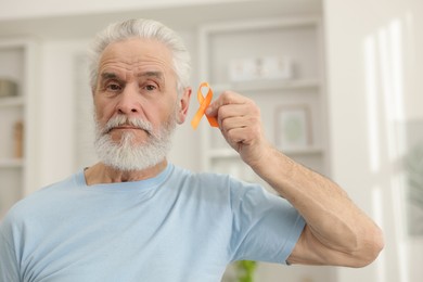 Photo of Multiple Sclerosis awareness. Senior man with orange ribbon indoors