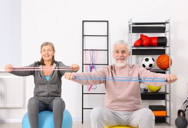 Photo of Smiling elderly couple exercising with elastic bands and fitness balls at home