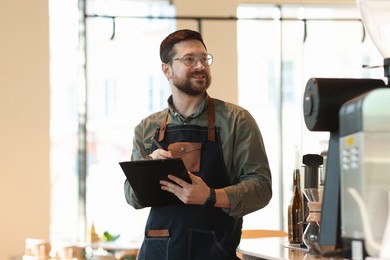 Photo of Smiling business owner working with clipboard in his cafe