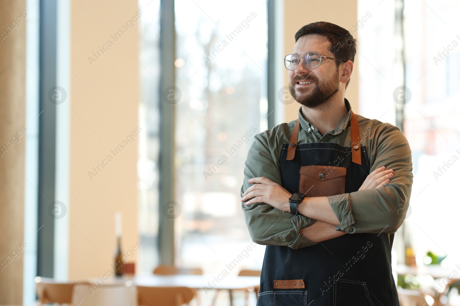 Photo of Smiling business owner with crossed arms in his cafe. Space for text