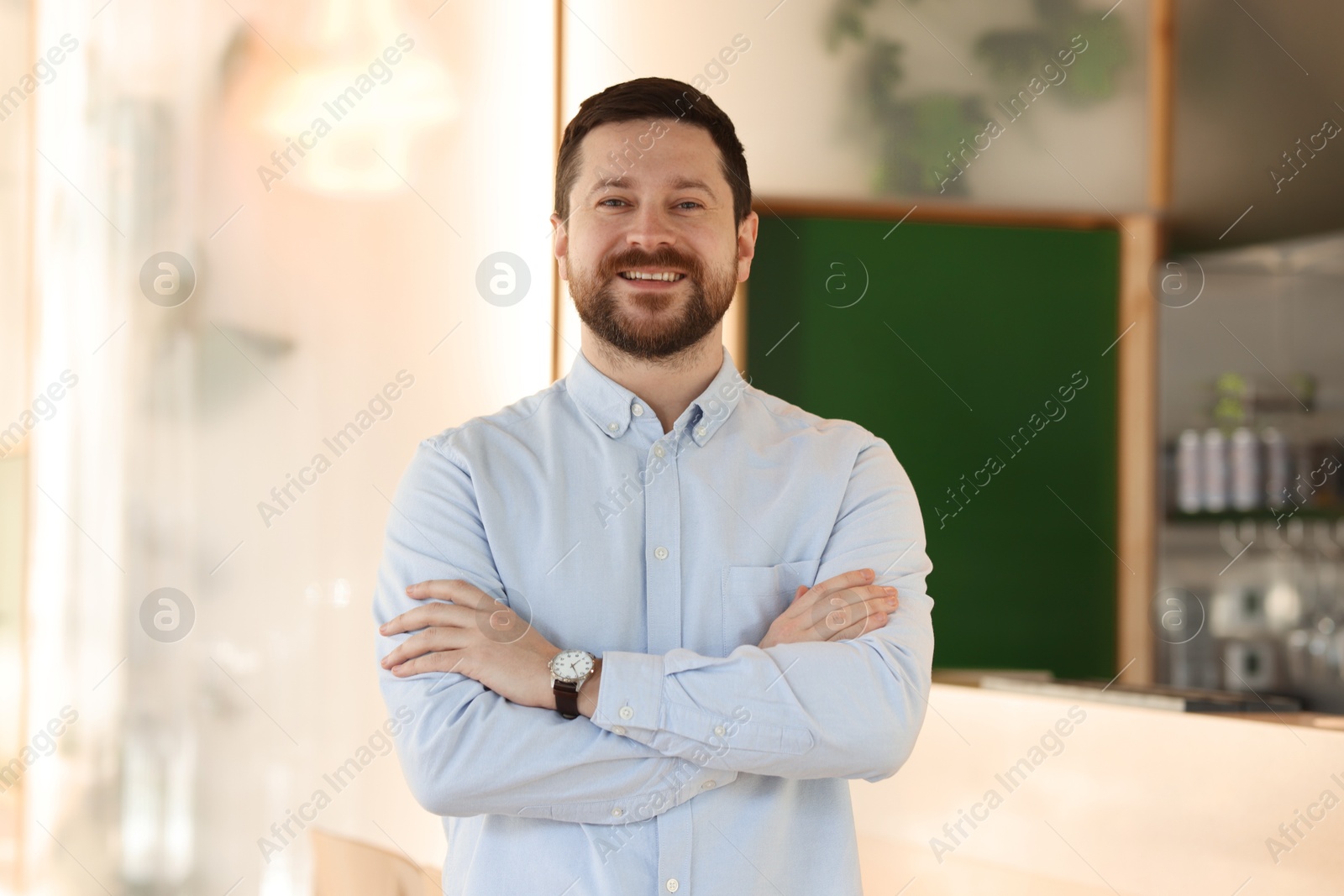 Photo of Portrait of smiling business owner with crossed arms in his cafe