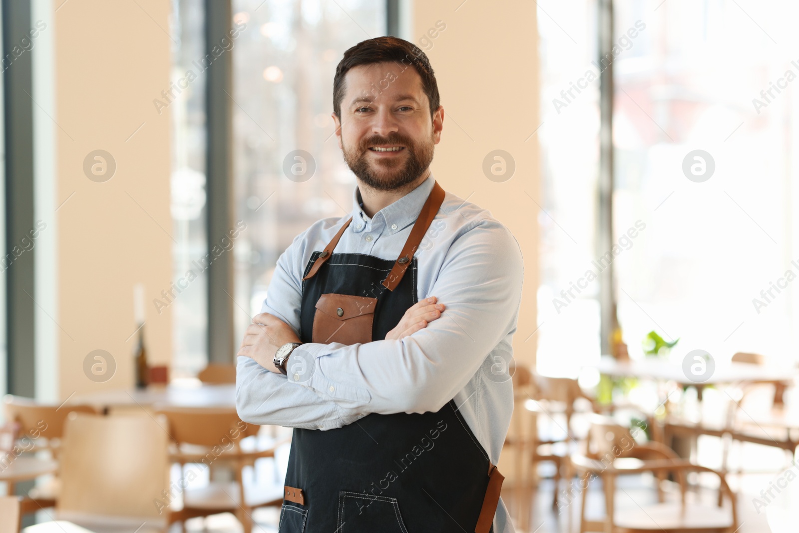 Photo of Portrait of smiling business owner with crossed arms in his cafe