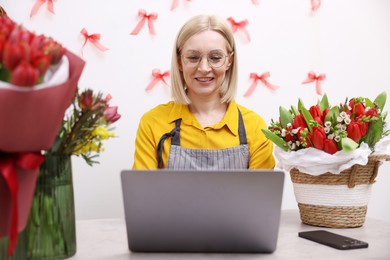 Photo of Business owner working on laptop at table in her flower shop