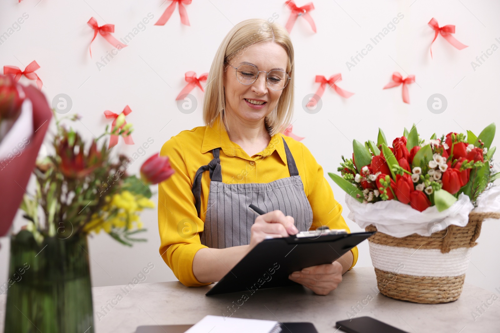 Photo of Business owner with clipboard taking notes at table in her flower shop