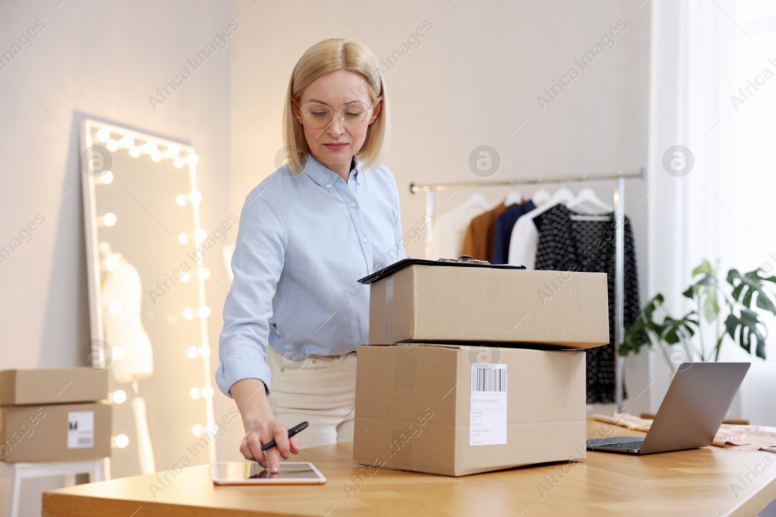 Photo of Business owner using tablet at table with parcels in her tailor shop