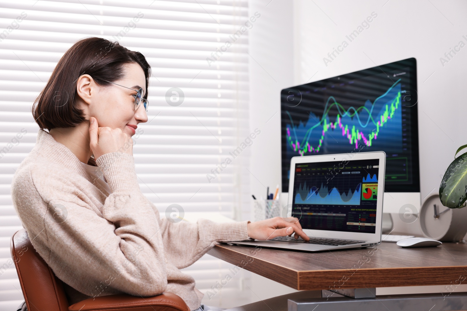 Photo of Stock exchange. Woman analysing financial market on laptop at wooden table indoors