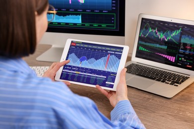 Photo of Stock exchange. Woman analysing financial market on tablet at wooden table indoors