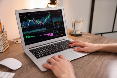 Photo of Stock exchange. Woman analysing financial market on laptop at wooden table indoors, closeup