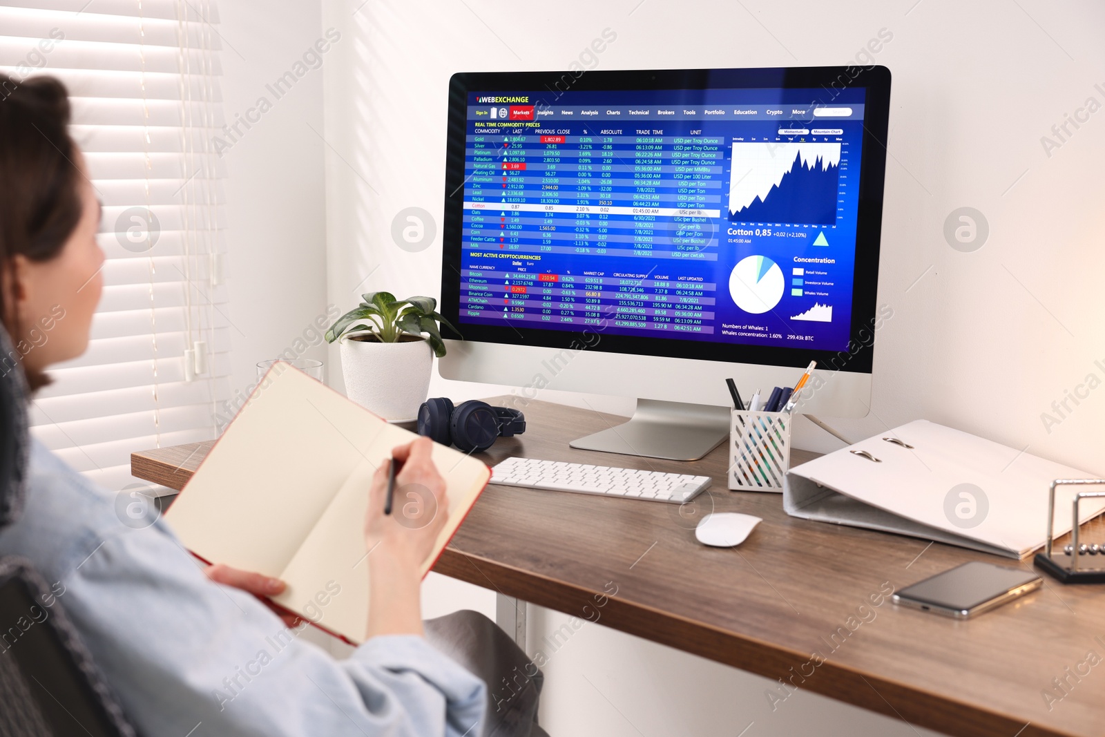 Photo of Stock exchange. Woman taking notes while analysing financial market on computer at wooden table indoors