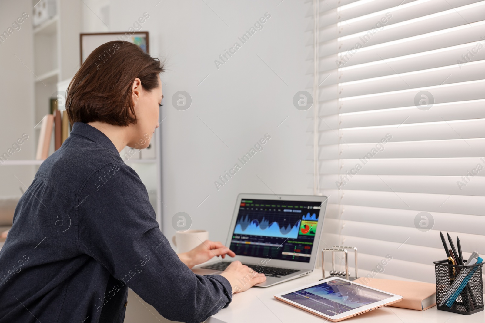 Photo of Stock exchange. Woman analysing financial market on laptop at white table indoors