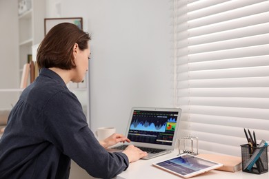 Photo of Stock exchange. Woman analysing financial market on laptop at white table indoors