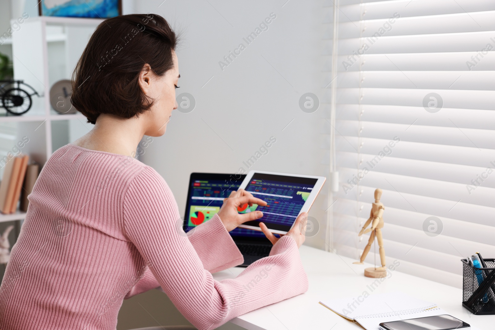 Photo of Stock exchange. Woman analysing financial market on tablet at white table indoors