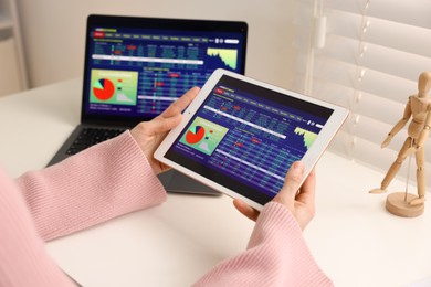 Photo of Stock exchange. Woman analysing financial market on tablet at white table indoors, closeup