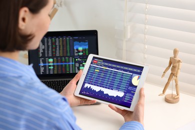 Photo of Stock exchange. Woman analysing financial market on tablet at white table indoors, closeup