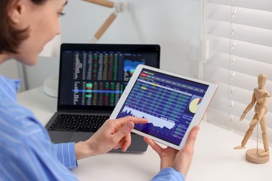 Photo of Stock exchange. Woman analysing financial market on tablet at white table indoors, closeup