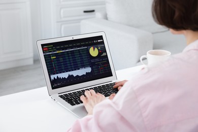 Photo of Stock exchange. Woman analysing financial market on laptop at white table indoors, closeup