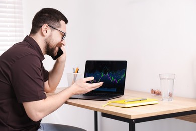 Photo of Stock exchange. Man talking on smartphone at desk indoors