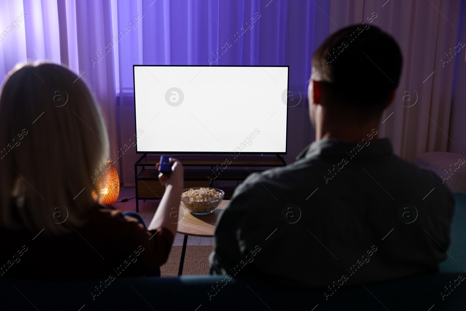 Photo of Lovely couple watching tv at home in evening, back view