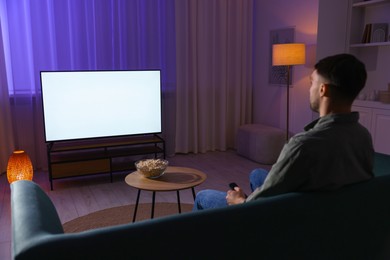 Photo of Man watching tv at home in evening, back view