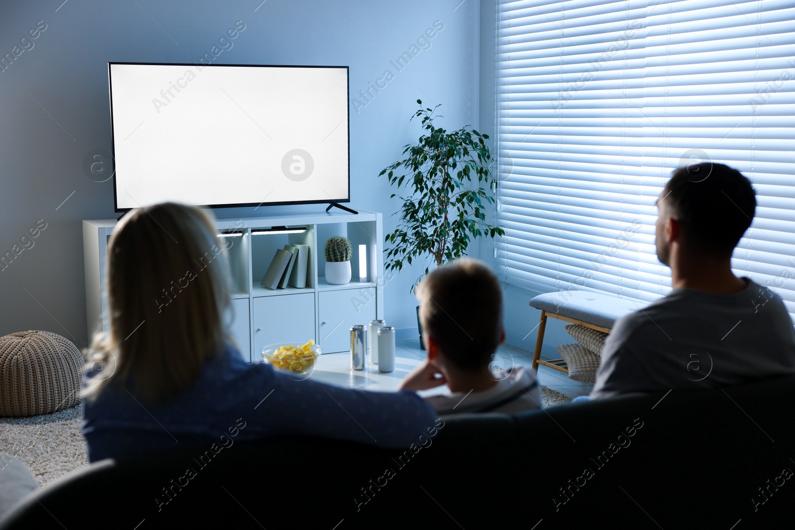 Photo of Happy family with snacks and drinks watching tv together at home, back view