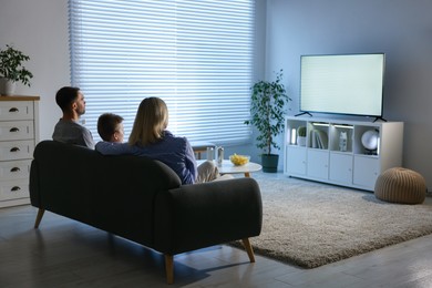 Photo of Happy family with snacks and drinks watching tv together at home