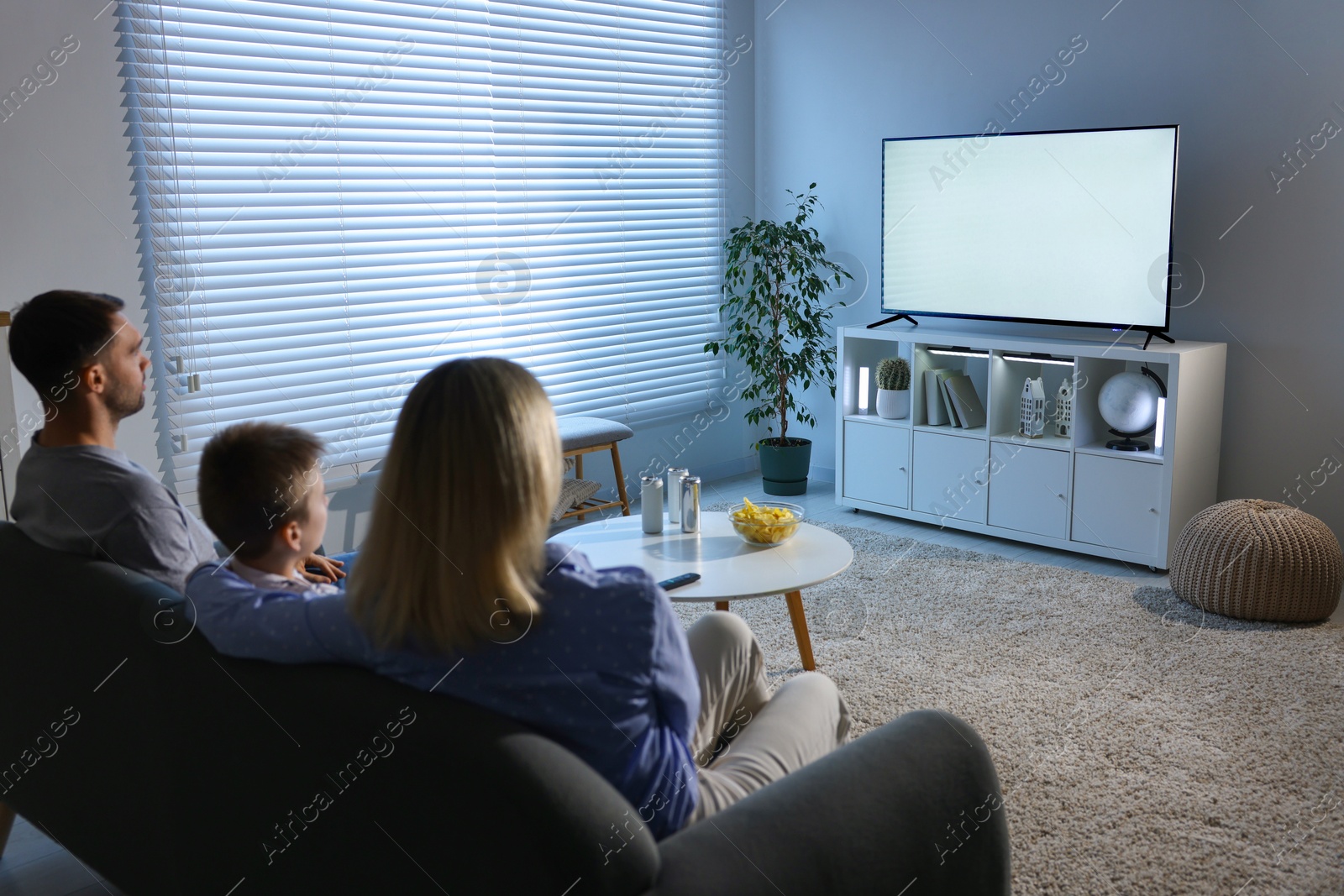 Photo of Happy family with snacks and drinks watching tv together at home