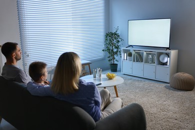 Photo of Happy family with snacks and drinks watching tv together at home