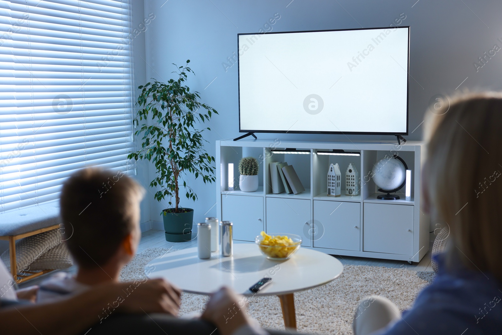 Photo of Happy family with snacks and drinks watching tv together at home, back view