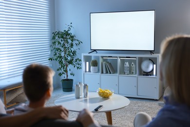 Photo of Happy family with snacks and drinks watching tv together at home, back view