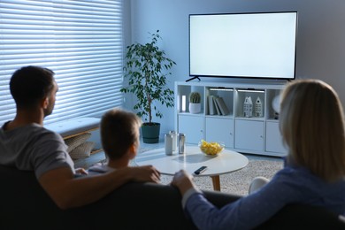 Photo of Happy family with snacks and drinks watching tv together at home, back view