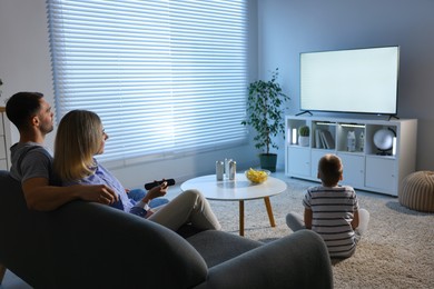 Photo of Happy family with snacks and drinks watching tv together at home