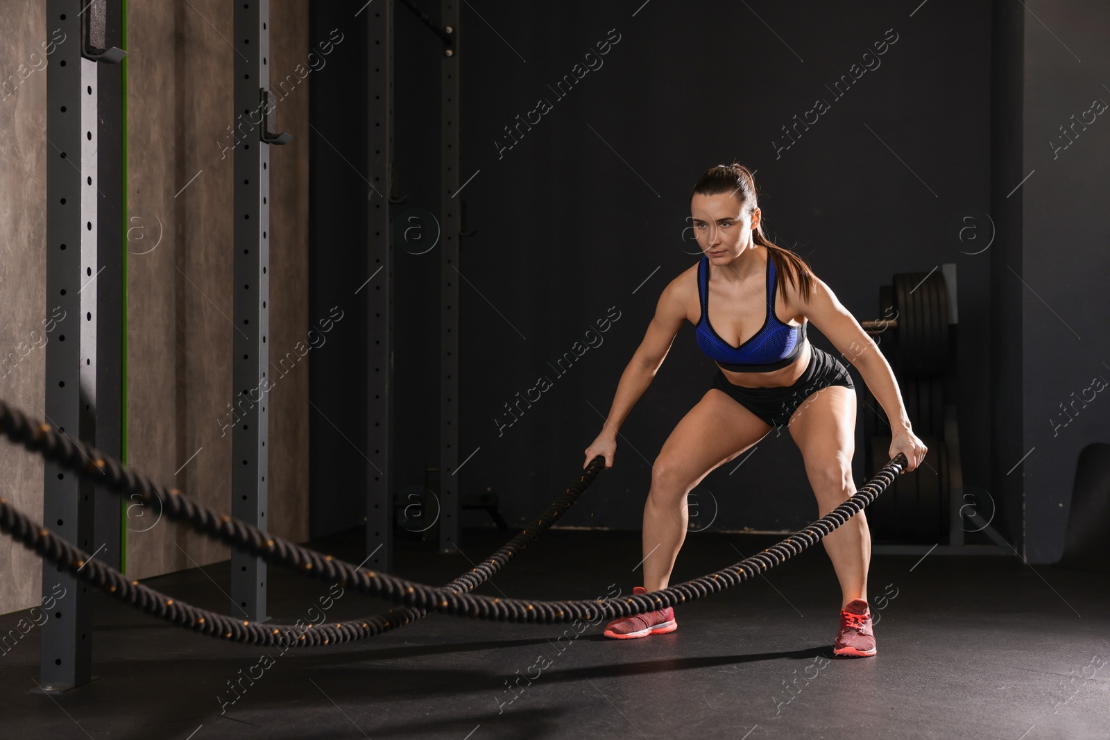 Photo of Sportswoman exercising with battle ropes during crossfit workout in gym. Space for text