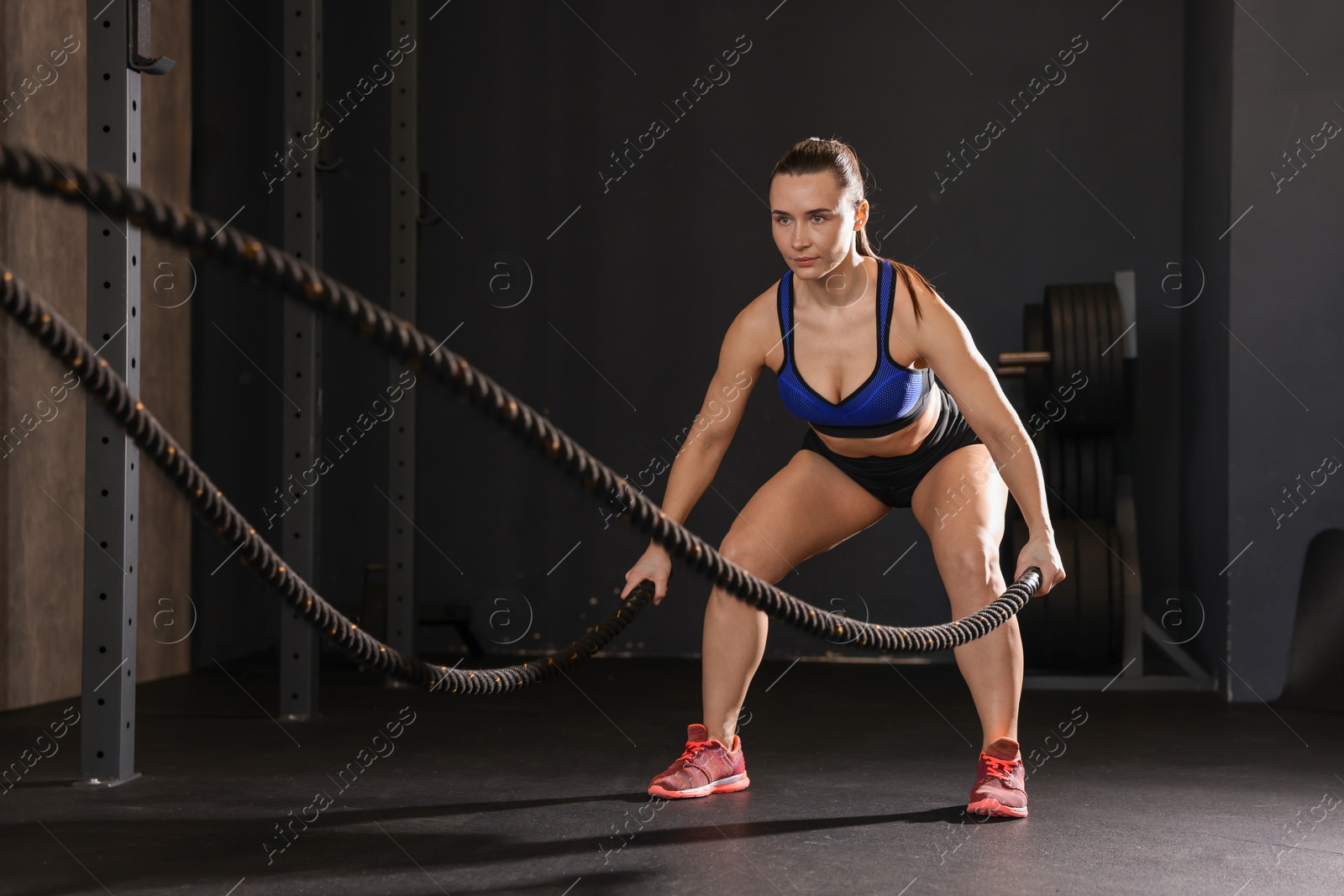 Photo of Sportswoman exercising with battle ropes during crossfit workout in gym