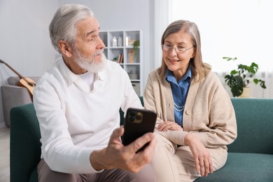 Photo of Happy elderly couple with smartphone on sofa at home