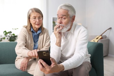 Photo of Cute elderly couple with smartphone on sofa at home