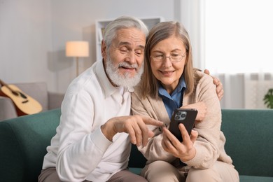 Photo of Happy elderly couple with smartphone on sofa at home