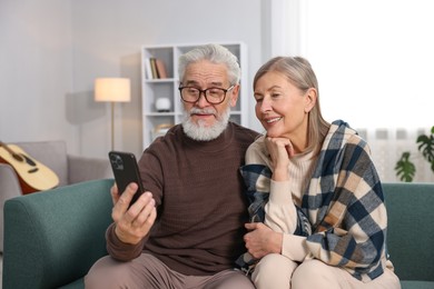 Photo of Happy elderly couple looking at smartphone on sofa at home