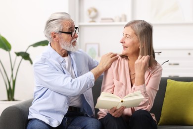 Photo of Cute elderly couple reading book together on sofa at home