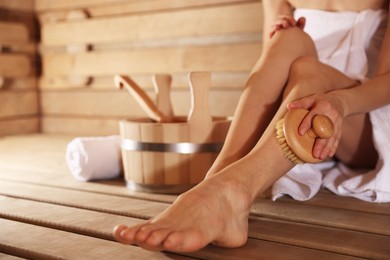 Photo of Woman massaging her leg with brush and bath supplies at sauna, closeup